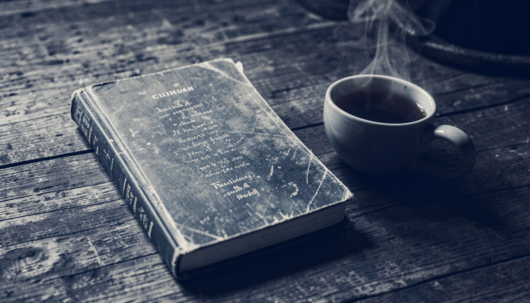 A worn hardcover poetry collection resting on a wooden table beside a steaming cup of tea, warm amber and deep navy tones