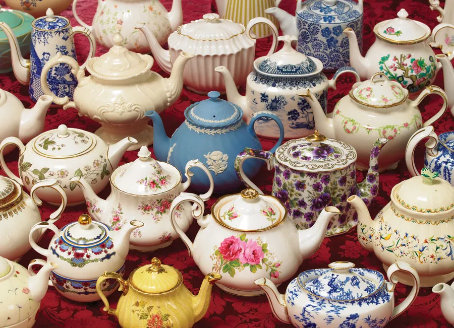 Overhead photo of many ornate porcelain teapots in varied patterns arranged on a red tablecloth